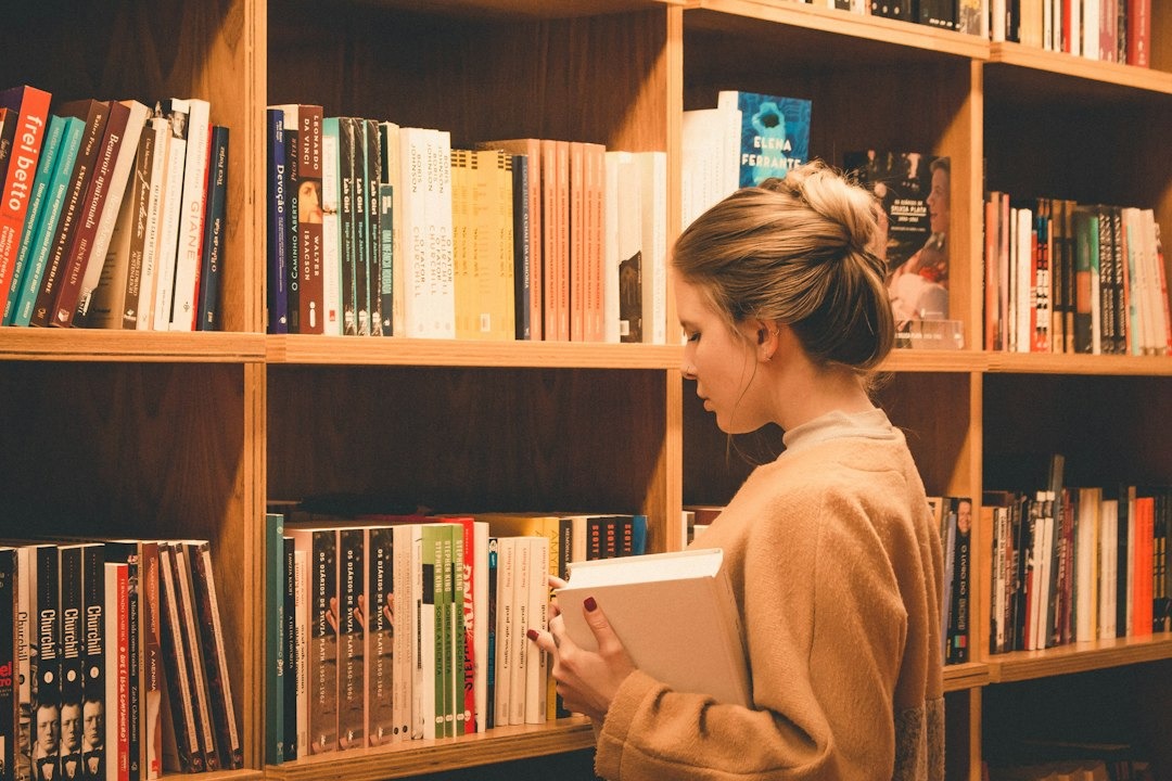 Woman in sweater reads book in a library.